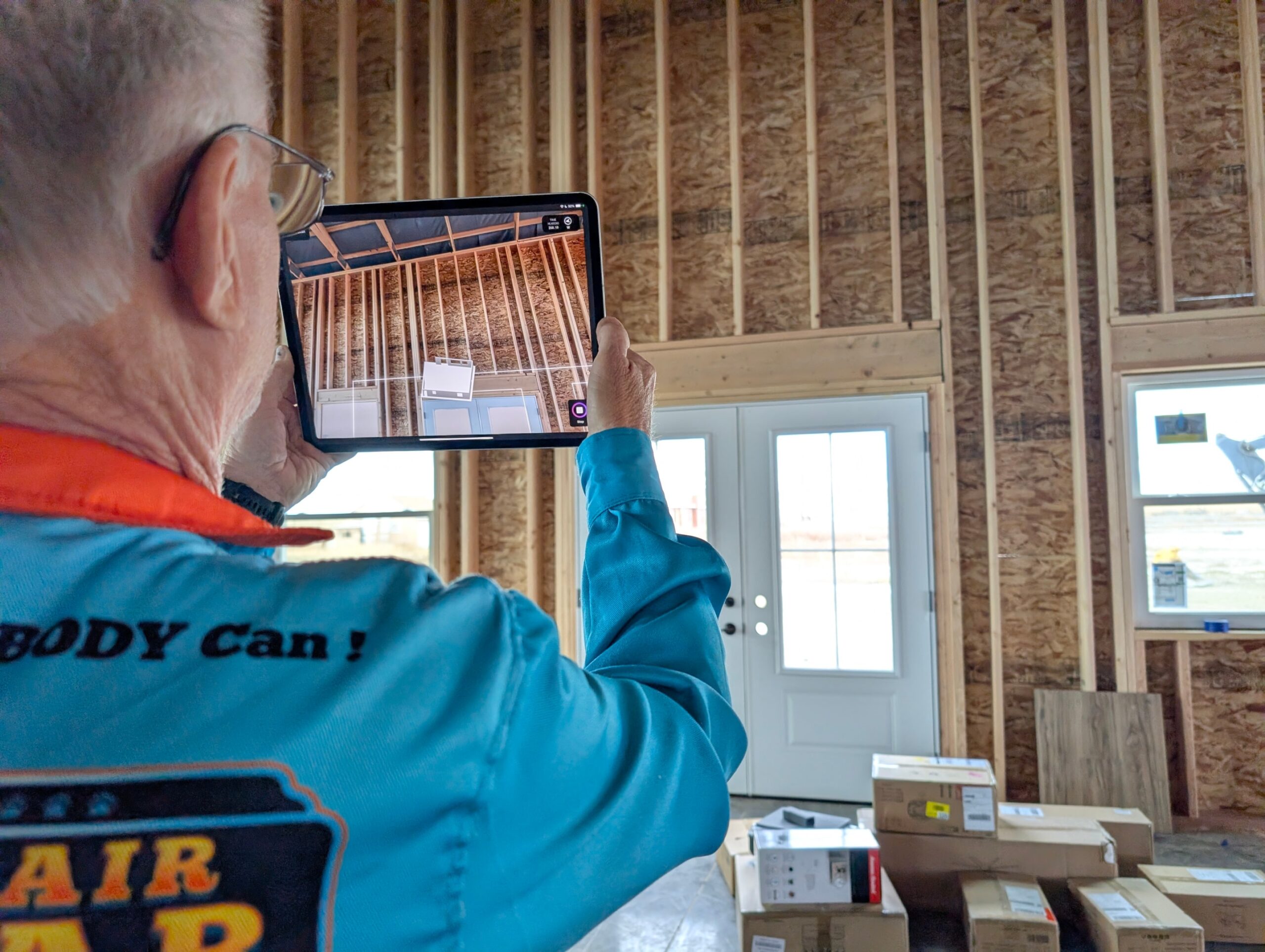 The image shows a technician performing a software load calculation scan in a new home that is still in the frame stage, highlighting the importance of correctly sizing HVAC systems to avoid issues like higher energy costs and inefficient operation. The technician is focused on ensuring the air conditioning and heating systems will operate efficiently once installed.